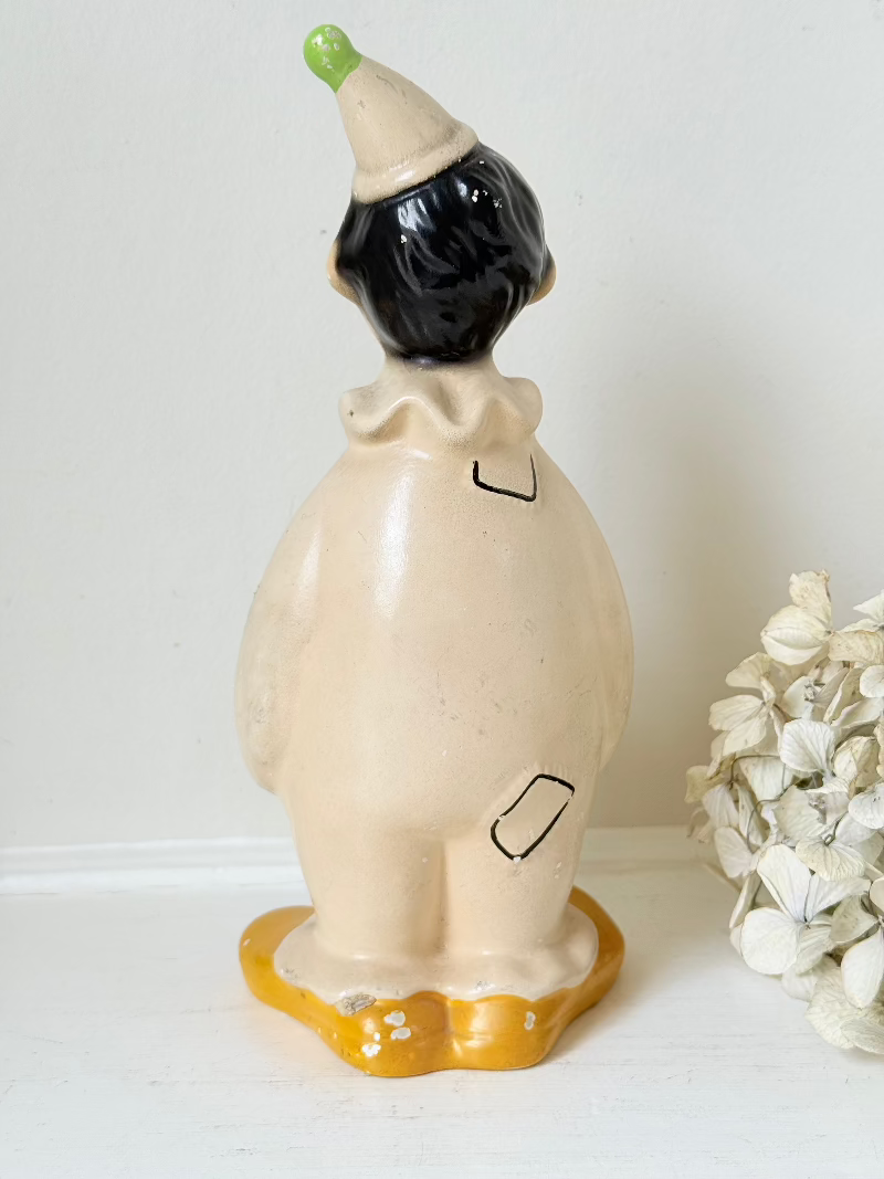 vintage ceramic clown moneybox with green and yellow painted details on white surface