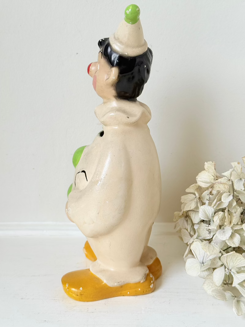 vintage ceramic clown moneybox with green and yellow painted details on white surface