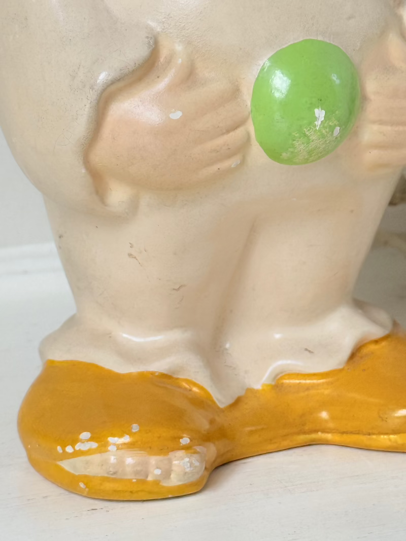 vintage ceramic clown moneybox with green and yellow painted details on white surface