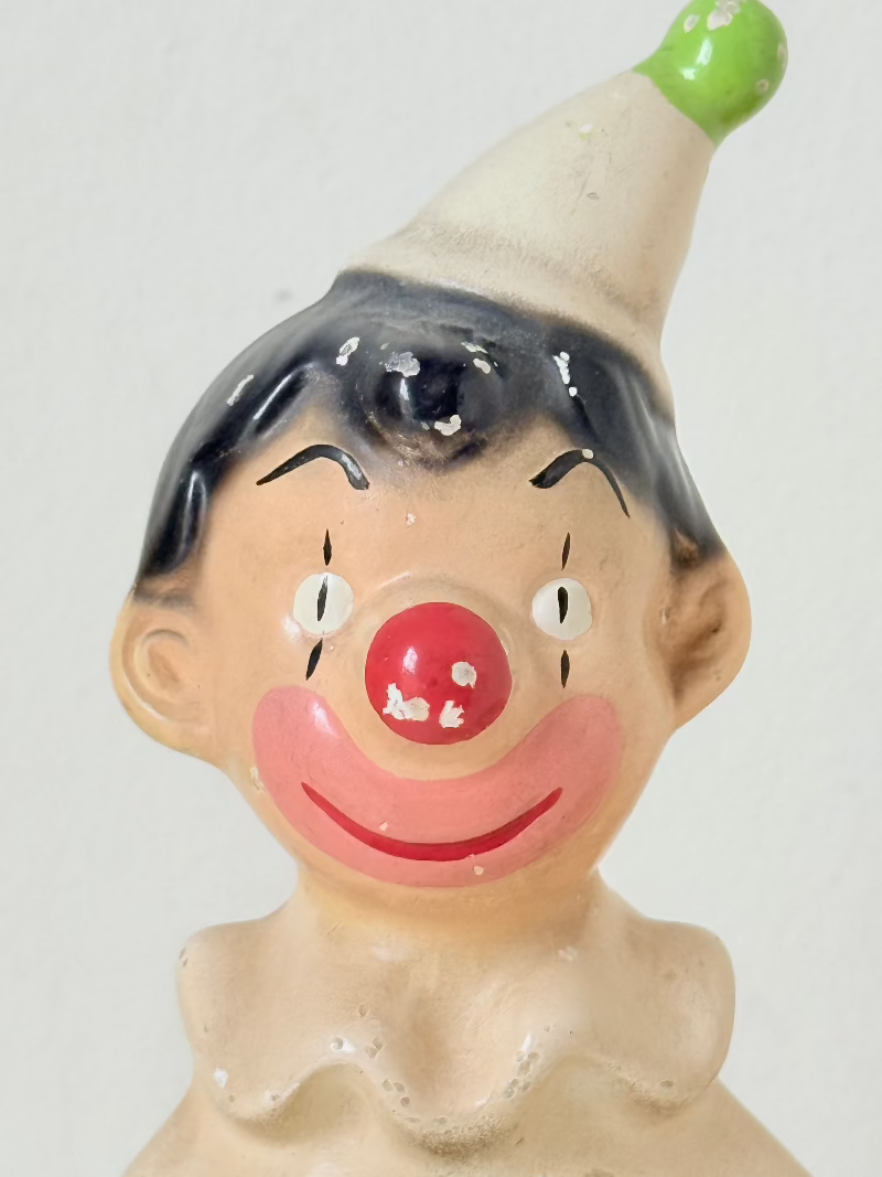 vintage ceramic clown moneybox with green and yellow painted details on white surface