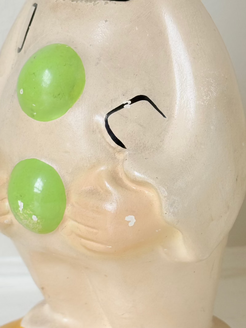 vintage ceramic clown moneybox with green and yellow painted details on white surface