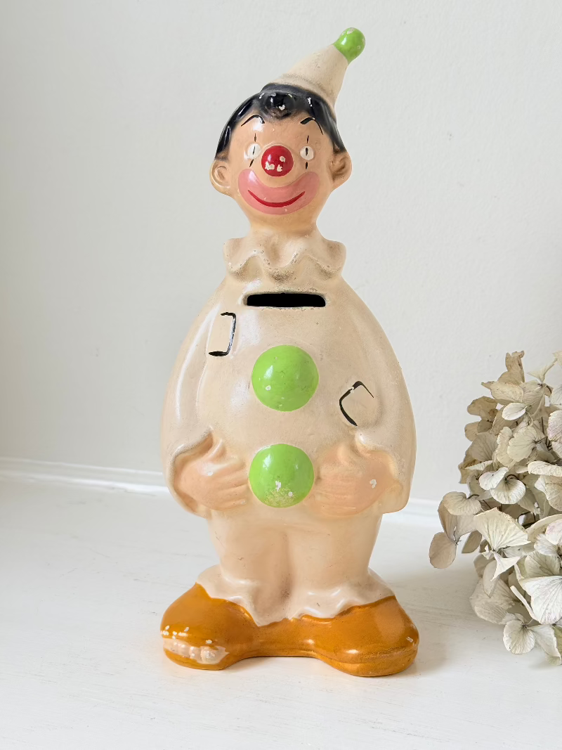 vintage ceramic clown moneybox with green and yellow painted details on white surface