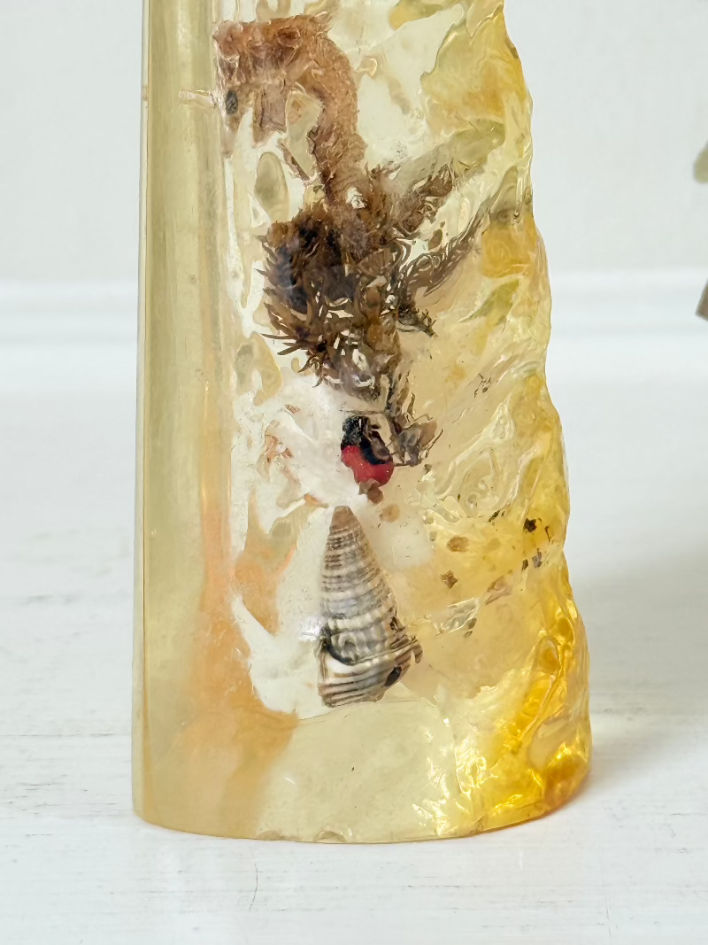 vintage 1970s resin bottle opener with embedded seashells and coastal treasures on white surface
