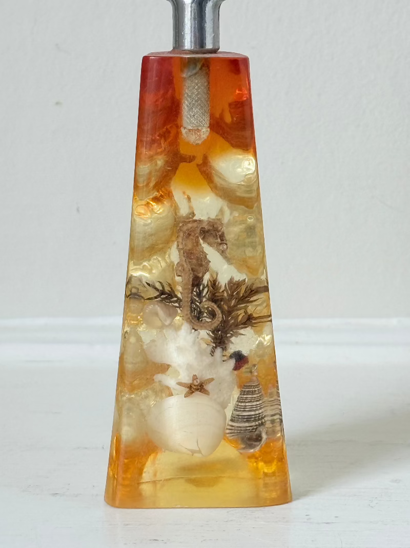 vintage 1970s resin bottle opener with embedded seashells and coastal treasures on white surface