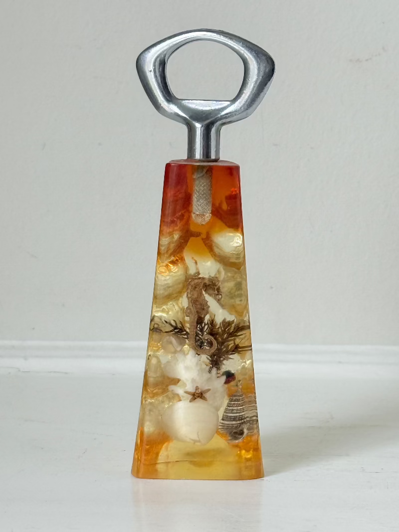 vintage 1970s resin bottle opener with embedded seashells and coastal treasures on white surface