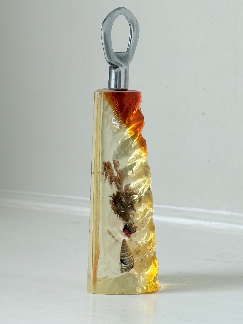 vintage 1970s resin bottle opener with embedded seashells and coastal treasures on white surface