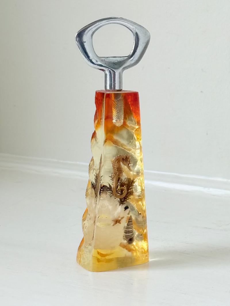 vintage 1970s resin bottle opener with embedded seashells and coastal treasures on white surface