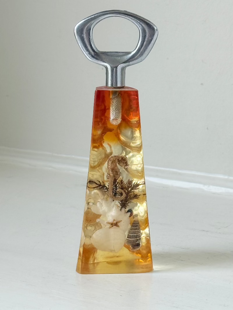 vintage 1970s resin bottle opener with embedded seashells and coastal treasures on white surface
