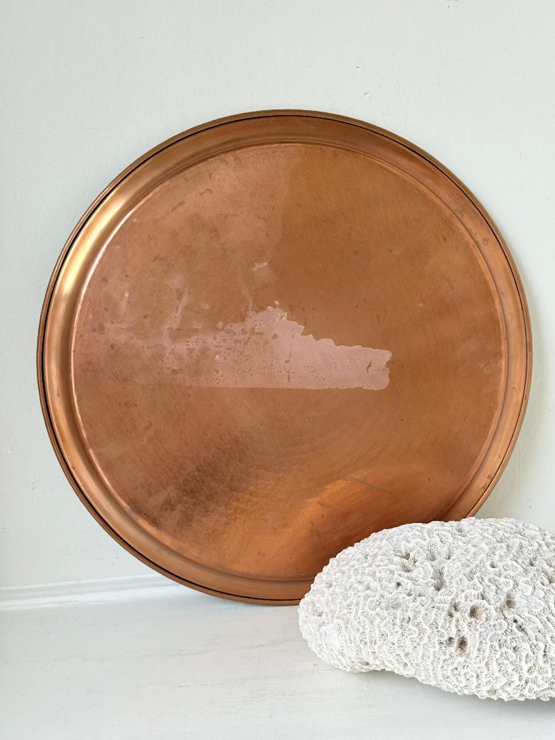 Lakeland Borrowdale hammered copper tray with warm patina, photographed on a white surface beside dried stems.