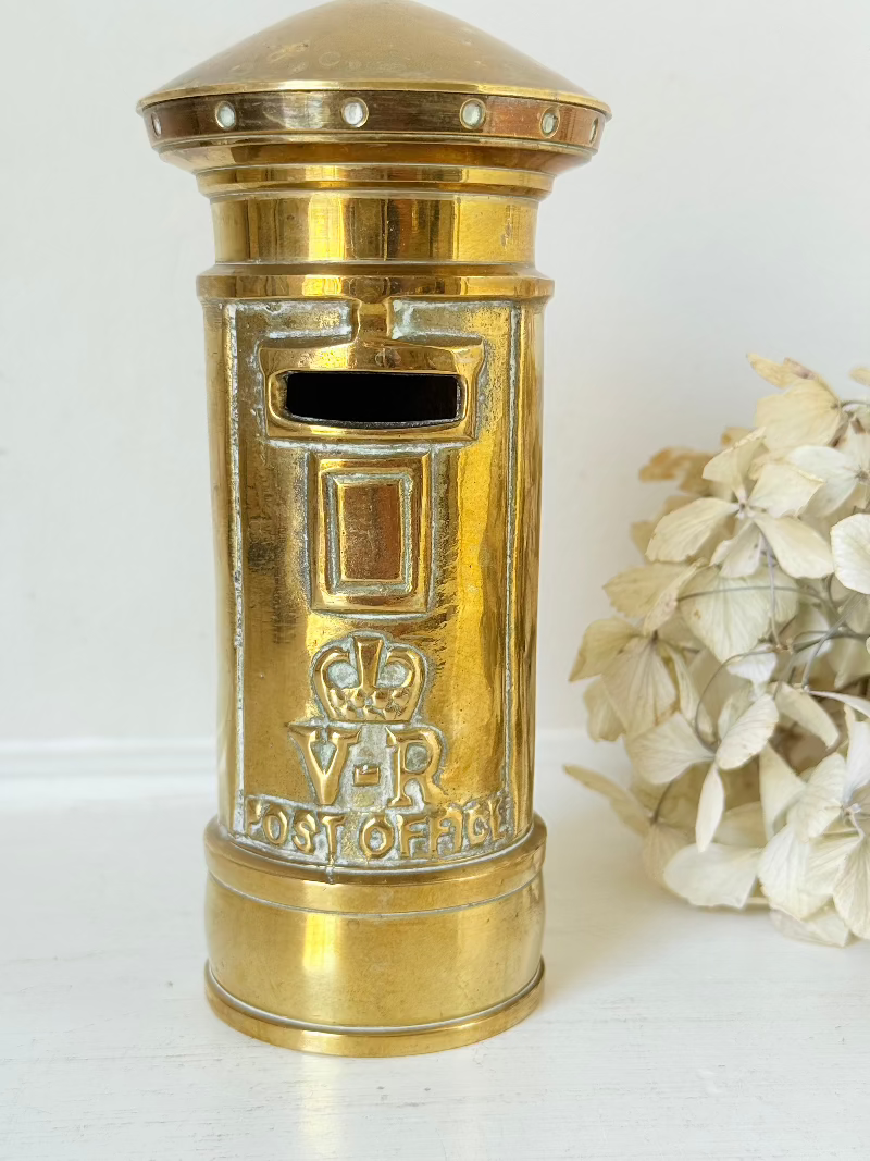 vintage brass post box moneybox with vr emblem photographed on white surface