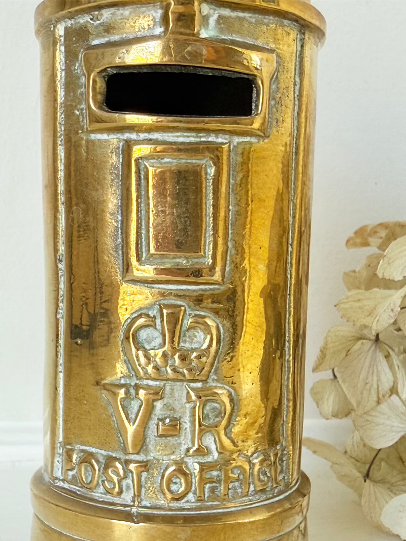 vintage brass post box moneybox with vr emblem photographed on white surface