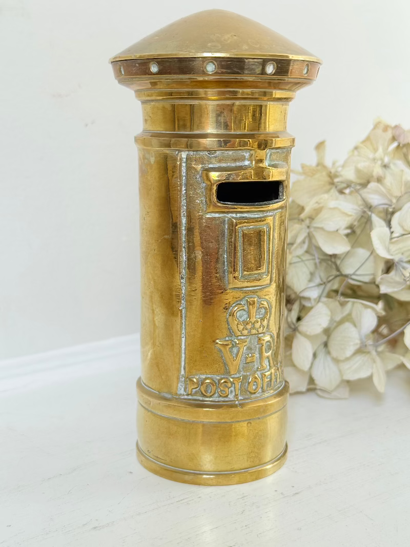 vintage brass post box moneybox with vr emblem photographed on white surface