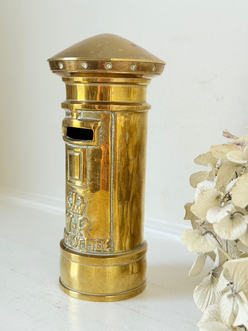 vintage brass post box moneybox with vr emblem photographed on white surface