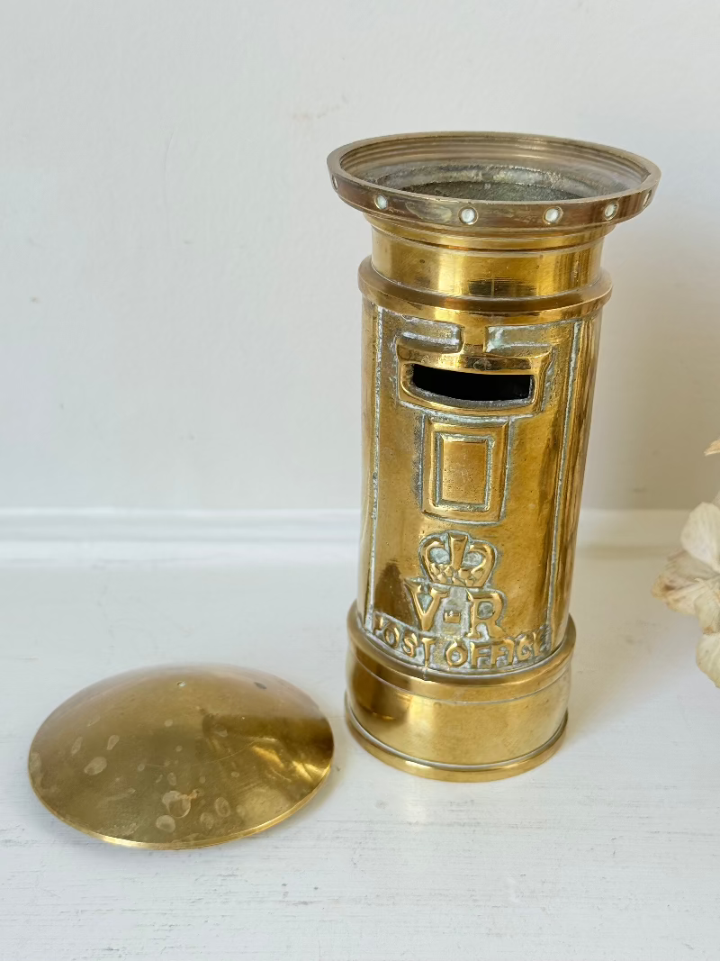 vintage brass post box moneybox with vr emblem photographed on white surface