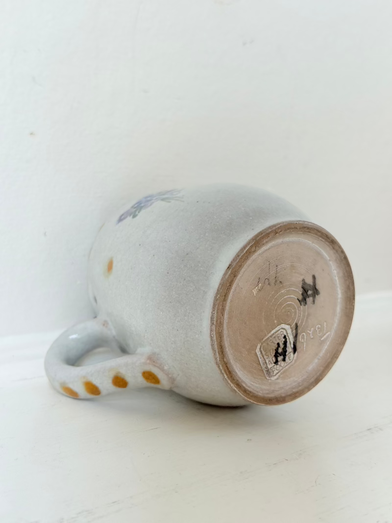 vintage studio pottery milk jug with hand painted lilac flowers and ochre rim photographed on white surface