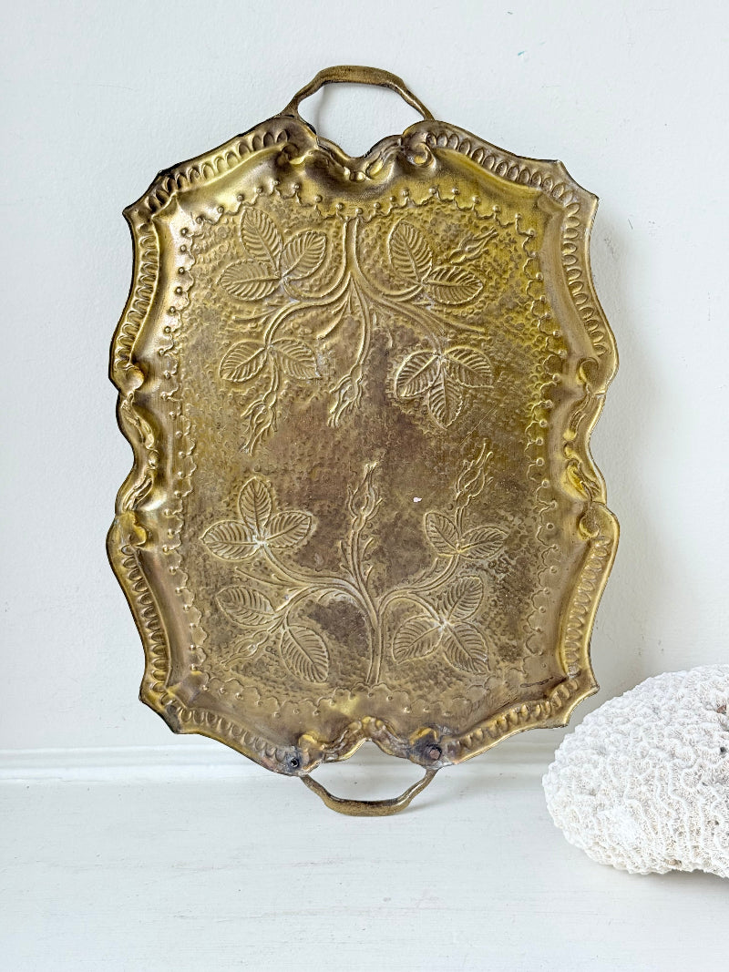 Vintage brass tray with embossed floral and leaf design, scalloped edge, and twin handles, photographed on a white surface