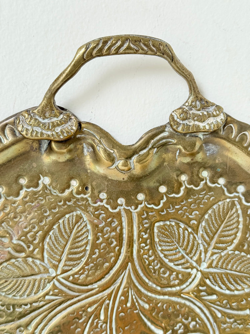 Vintage brass tray with embossed floral and leaf design, scalloped edge, and twin handles, photographed on a white surface
