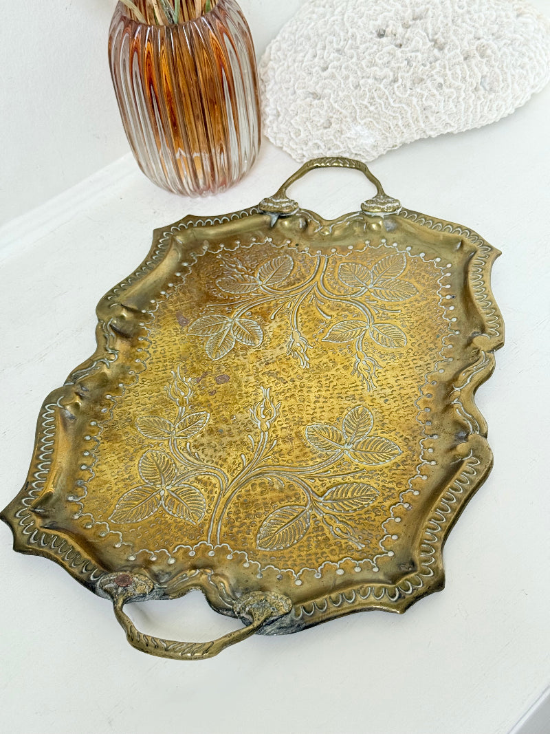 Vintage brass tray with embossed floral and leaf design, scalloped edge, and twin handles, photographed on a white surface