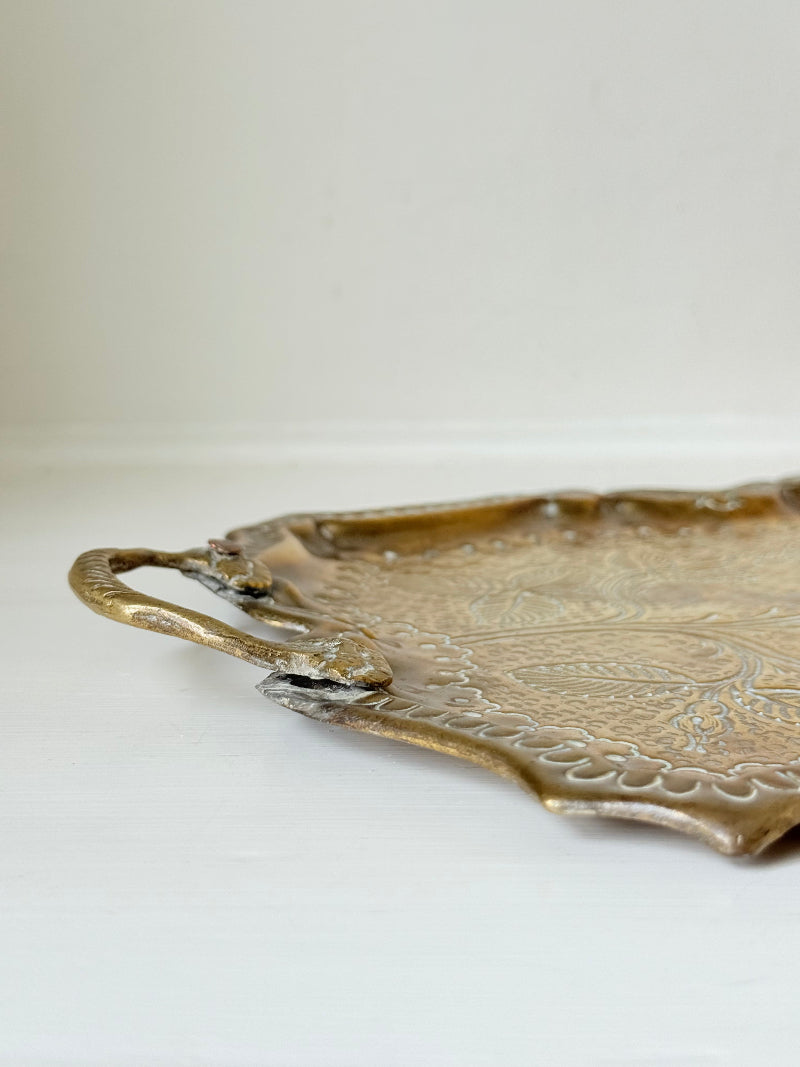 Vintage brass tray with embossed floral and leaf design, scalloped edge, and twin handles, photographed on a white surface