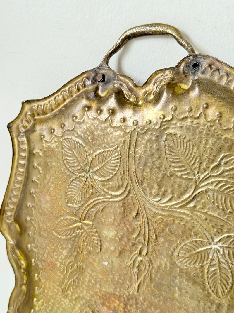 Vintage brass tray with embossed floral and leaf design, scalloped edge, and twin handles, photographed on a white surface