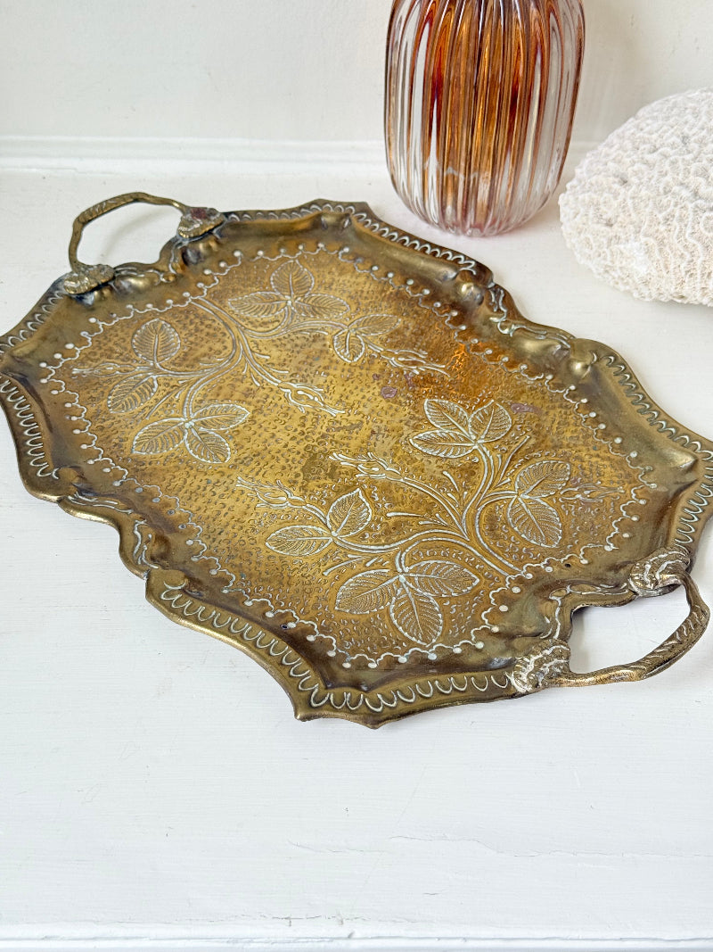 Vintage brass tray with embossed floral and leaf design, scalloped edge, and twin handles, photographed on a white surface