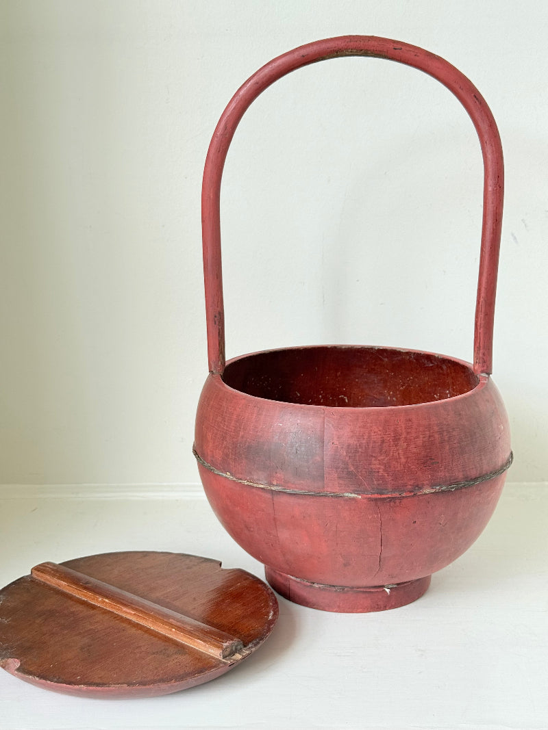 Vintage red painted wooden basket with tall curved handle and domed lid photographed on a white surface