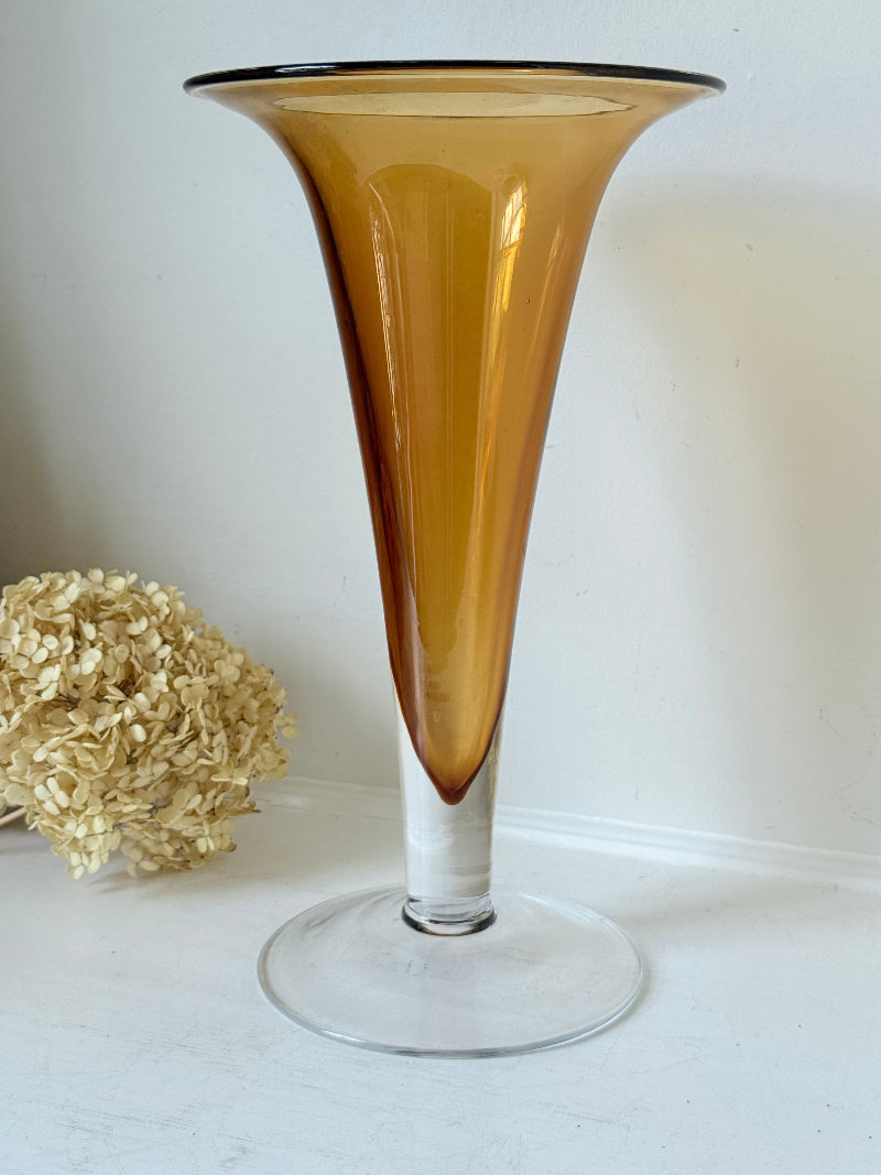 Tall mid-century amber trumpet vase with flared rim and clear glass foot, styled against a neutral background