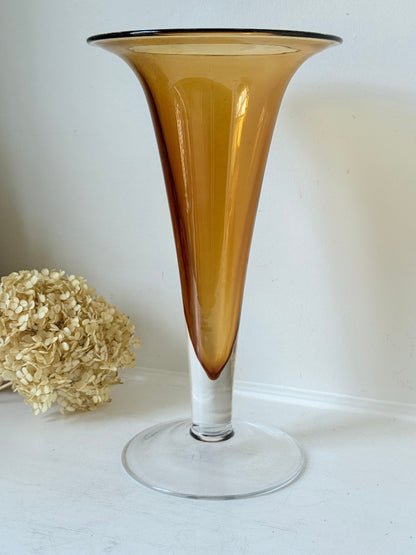Tall mid-century amber trumpet vase with flared rim and clear glass foot, styled against a neutral background