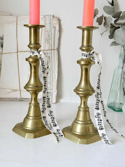 Pair of antique brass candlesticks with turned baluster stems and stepped bases holding coral tapers