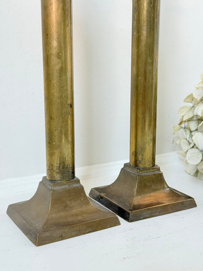 Pair of vintage brass candlesticks with square bases and white taper candles, styled on a white surface beside dried hydrangeas.
