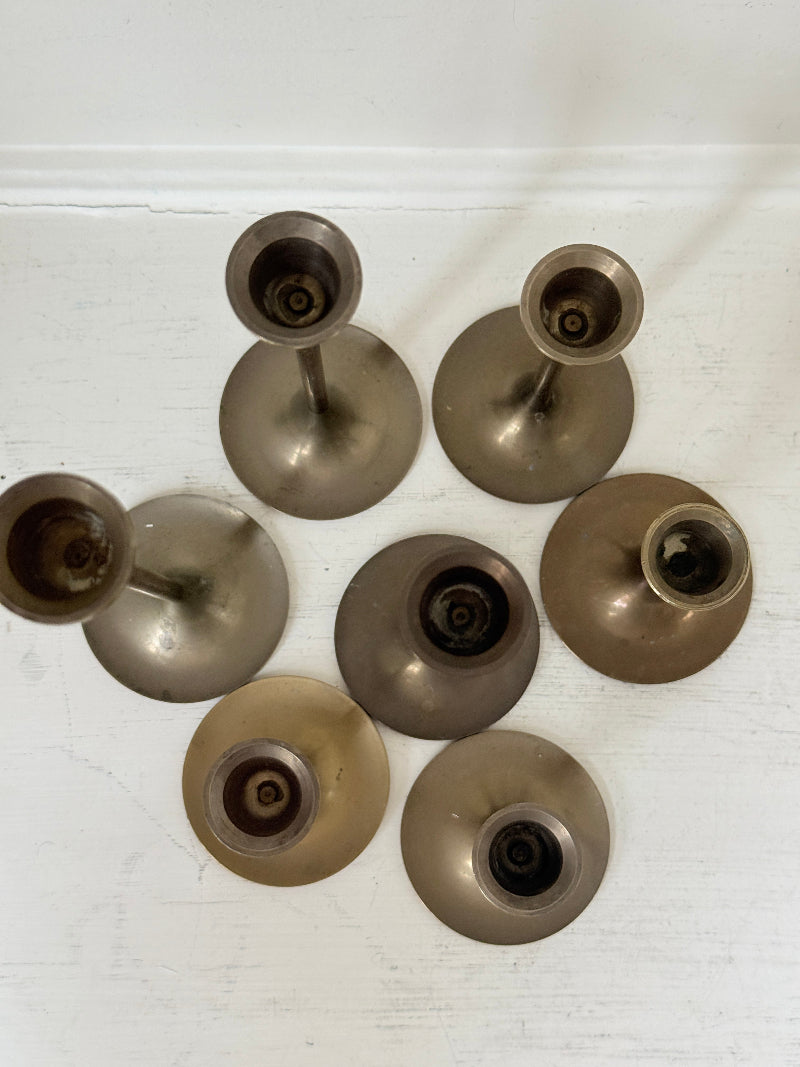 Set of 7 vintage brass candlesticks in graduated heights with aged brass finish styled with red ribbon on white surface