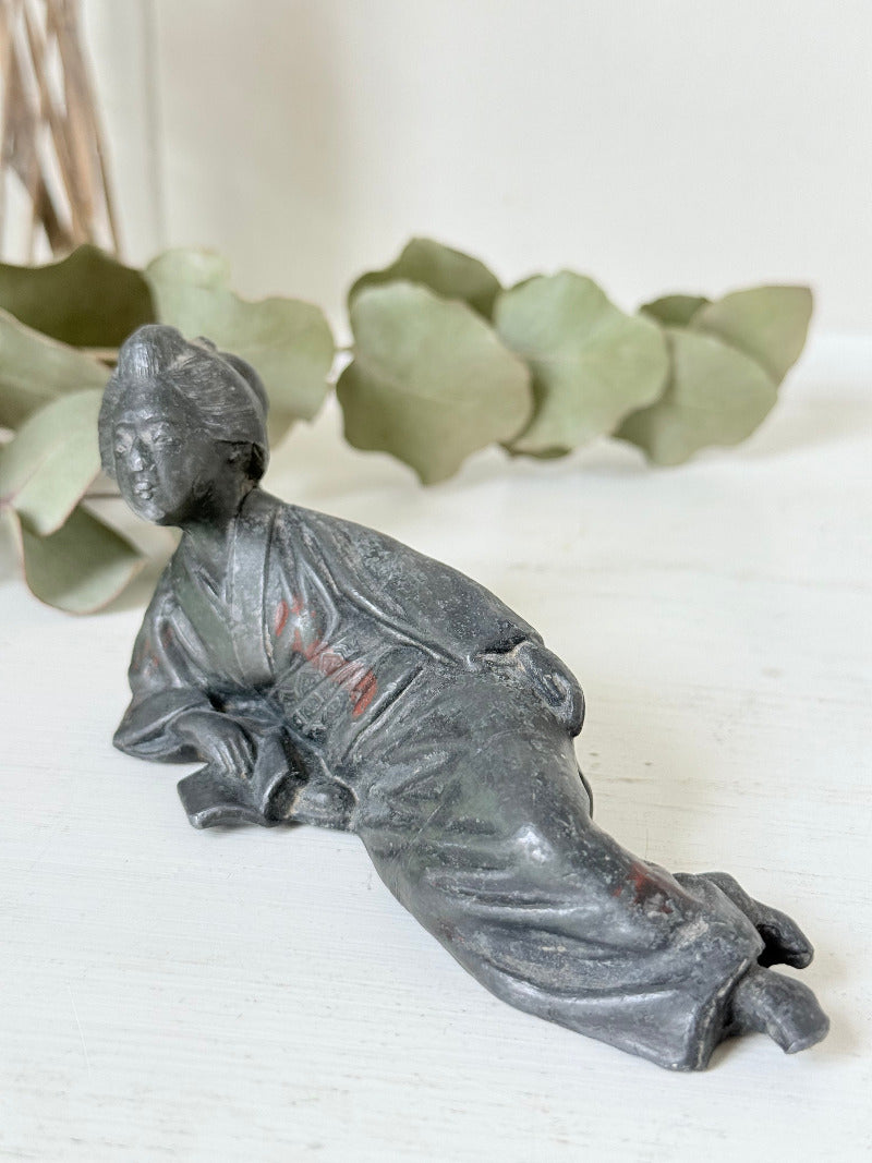 antique japanese bronze reclining lady with impressed marks to base photographed on white surface with foliage background