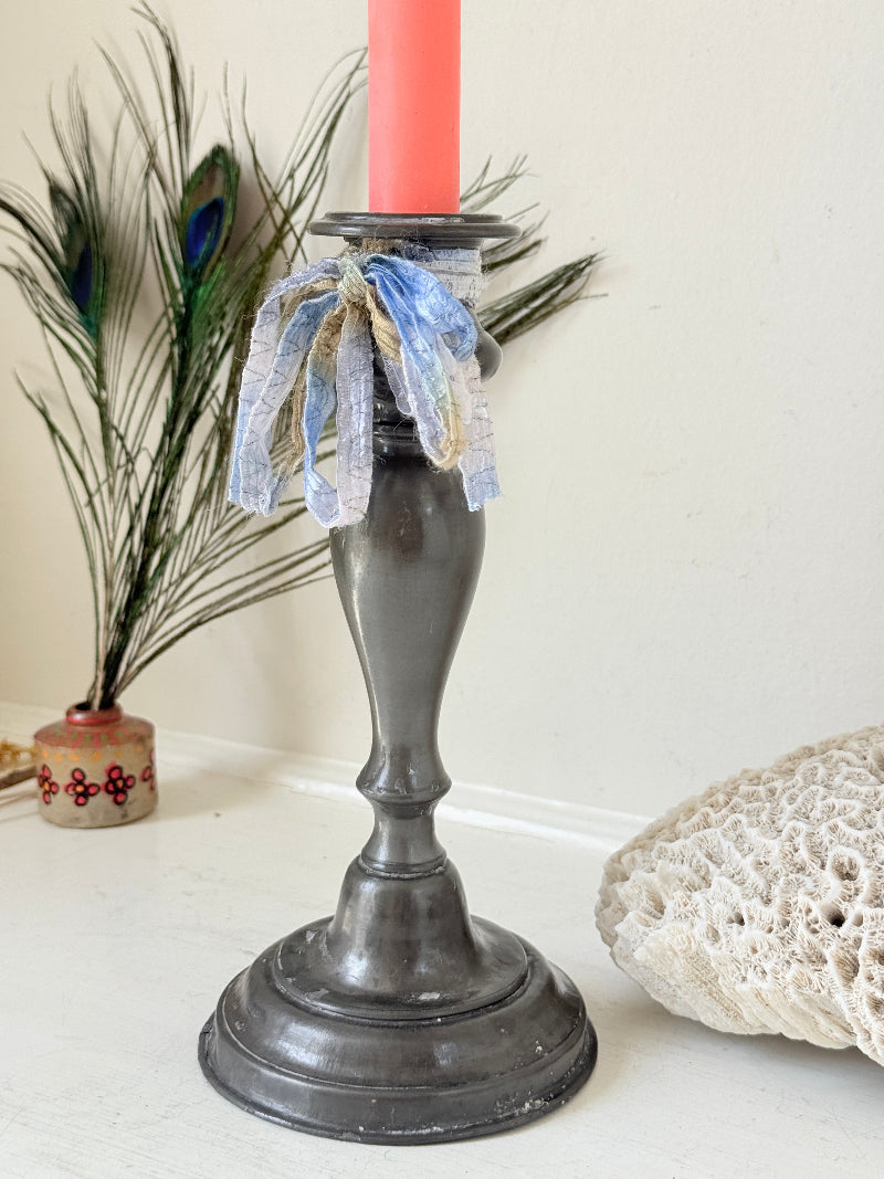 Antique pewter candlestick with baluster stem and aged patina styled with coral candle on white surface