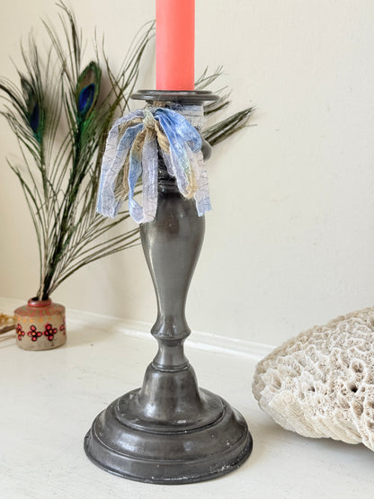 Antique pewter candlestick with baluster stem and aged patina styled with coral candle on white surface