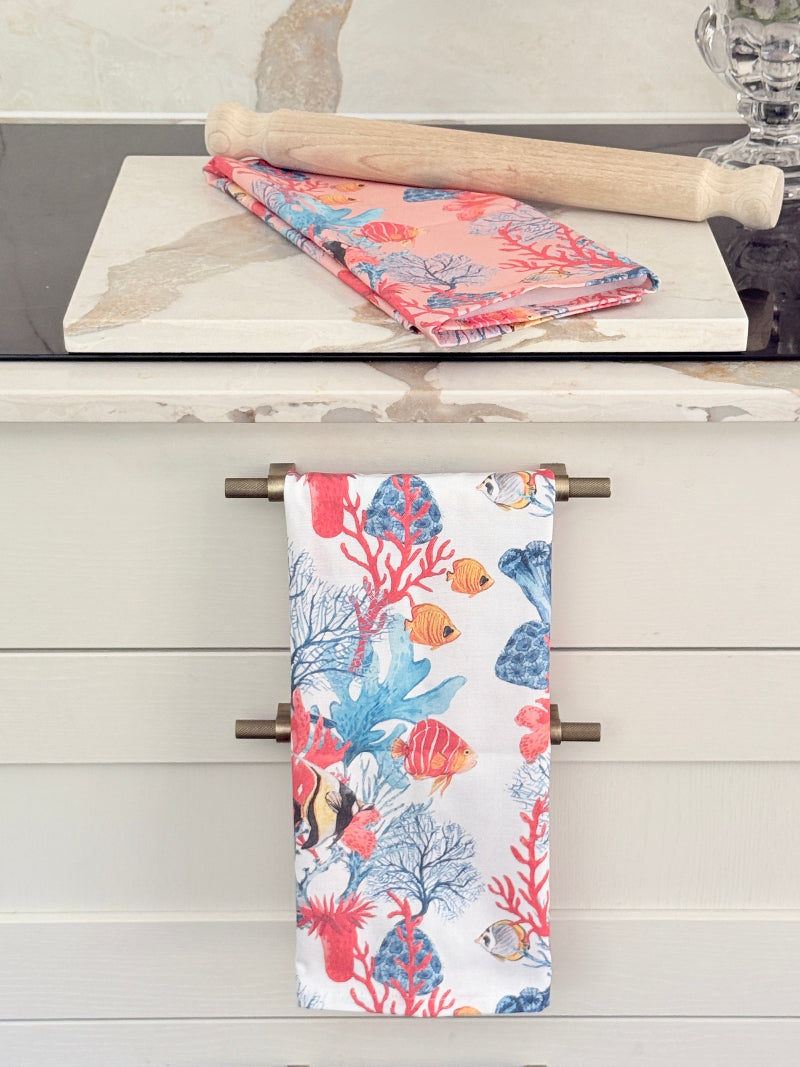 Coral reef and fish print cotton tea towel on a crisp white ground draped over a rail with marble and a rolling pin