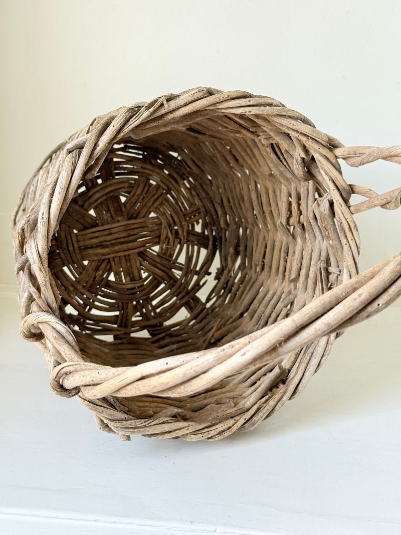 Rustic vintage wicker basket with woven handle and aged natural finish photographed on a white surface
