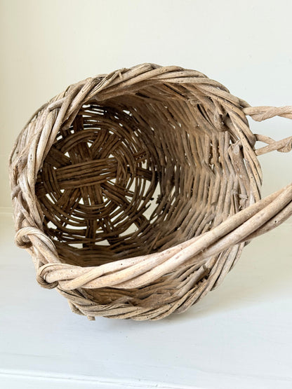Rustic vintage wicker basket with woven handle and aged natural finish photographed on a white surface