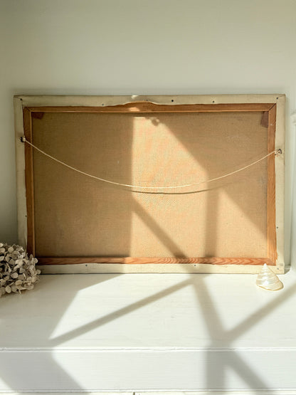 The back of a rectangular framed canvas or print, showing a tan linen ground, wooden frame, and hanging cord, resting on a white shelf with natural window shadows.