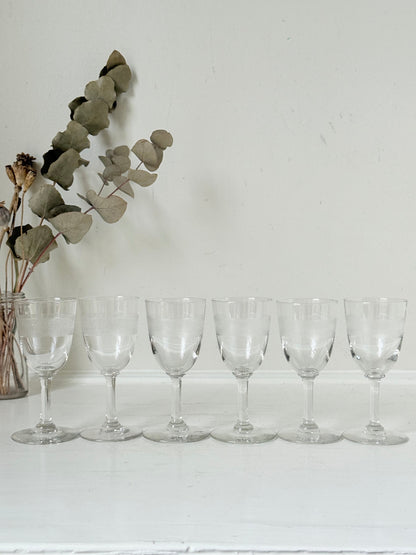 Set of six vintage etched clear glasses with decorative banding, one with a tiny rim chip, photographed on white surface.