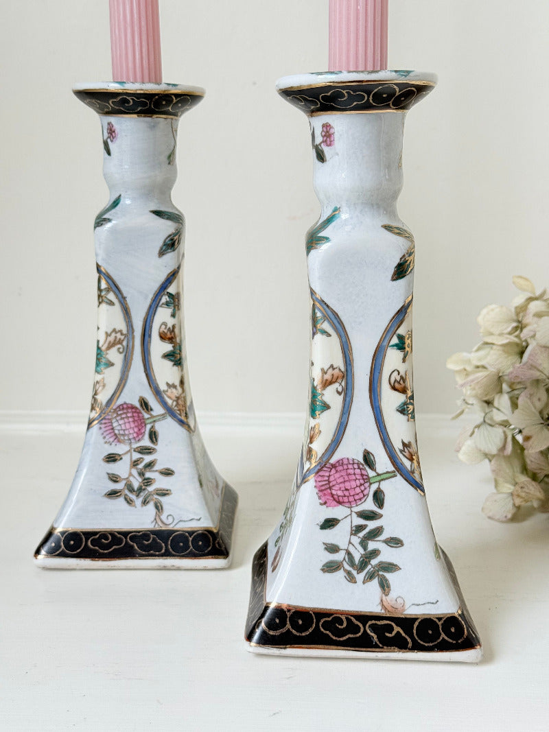 Pair of porcelain candle holders with hand-painted floral and vase motif in muted greens, pinks, and gold, styled with blush pink taper candles.