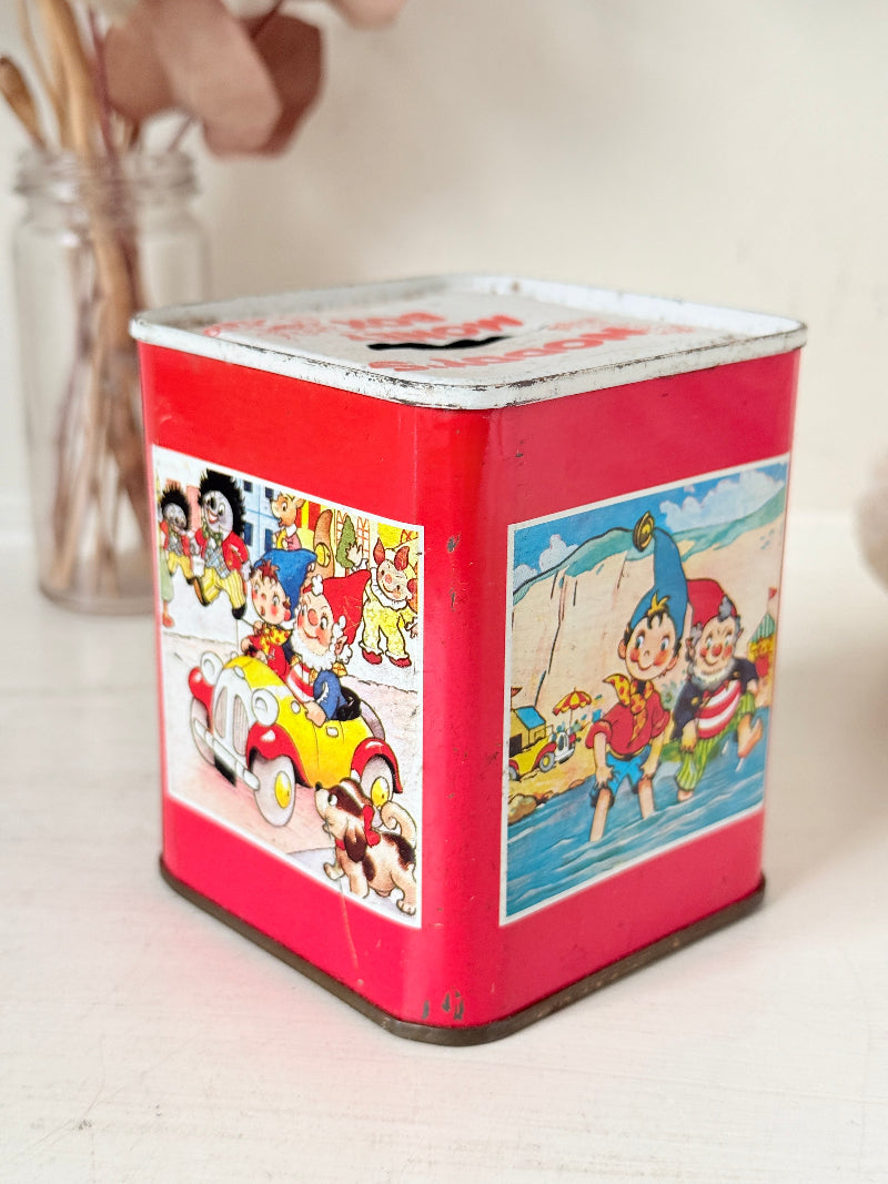 Vintage Noddy money box tin in red with illustrated panels, photographed on a white surface