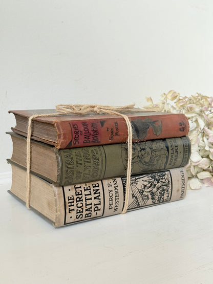 Vintage decorative book bundle in red, olive green and cream tied with twine, photographed on a white surface