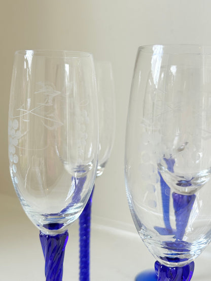 Set of six vintage French champagne flutes with tall clear bowls and cobalt blue twisted stems, photographed on white surface.