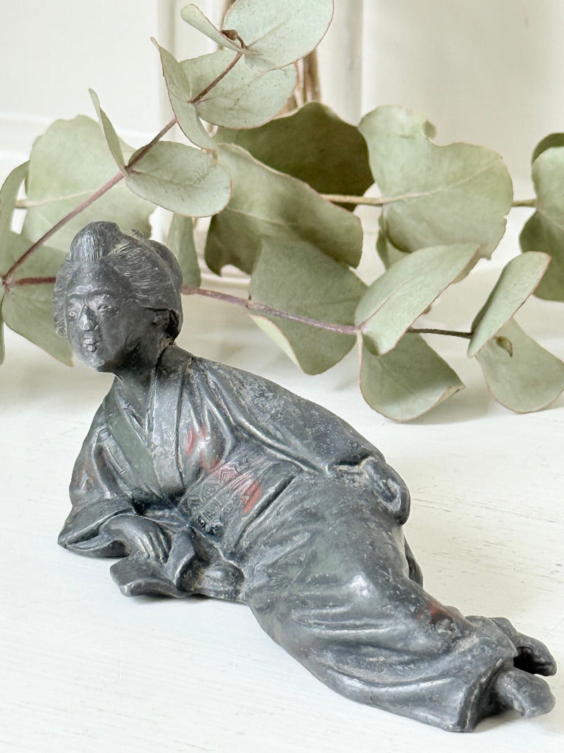 antique japanese bronze reclining lady with impressed marks to base photographed on white surface with foliage background