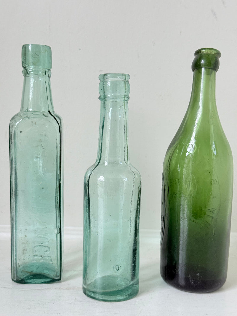 Trio of antique aqua and green glass bottles with embossed lettering, photographed on a white surface