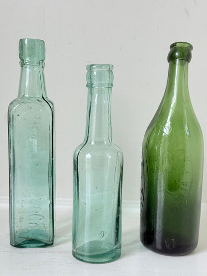 Trio of antique aqua and green glass bottles with embossed lettering, photographed on a white surface