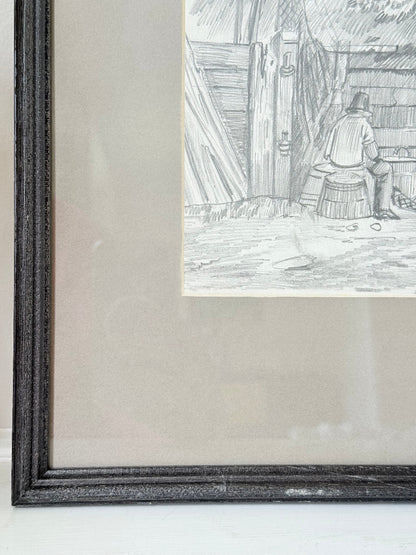 Vintage pencil drawing of rural scene with outbuildings and figures, under glass in black wooden frame, photographed on white surface.