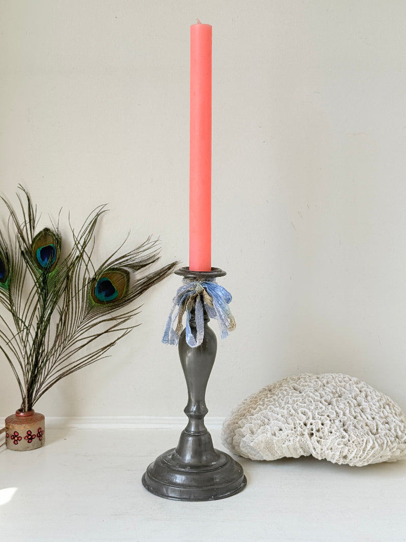 Antique pewter candlestick with baluster stem and aged patina styled with coral candle on white surface