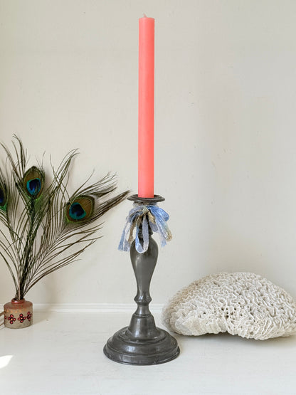 Antique pewter candlestick with baluster stem and aged patina styled with coral candle on white surface