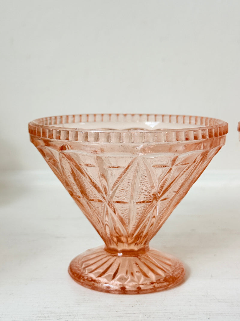 A vintage pink cut-glass pedestal bowl with a fluted rim and geometric diamond pattern, set against a plain off-white background.